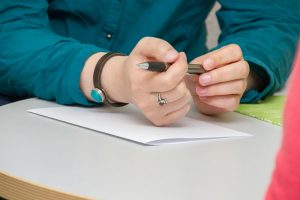 A woman diligently writes on a piece of paper, focused on her task with a pen in hand