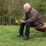 a old man is siting in the garden with the book