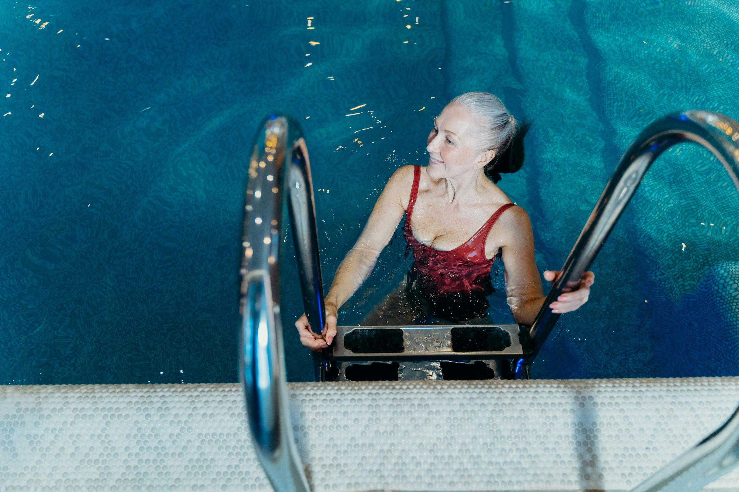 Elderly woman in a red swimsuit smiling while exiting a swimming pool